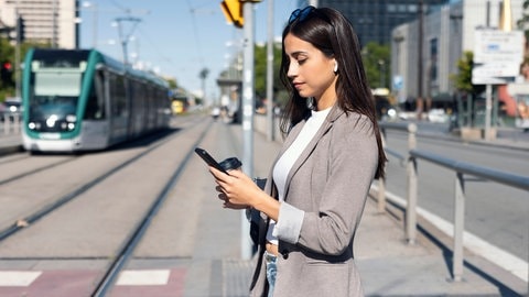 Frau mit Smartphone an der Haltestelle: Viele Apps greifen Standortdaten vom Handy ab und leiten sie weiter