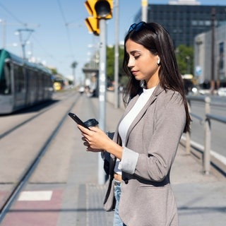 Frau mit Smartphone an der Haltestelle: Viele Apps greifen Standortdaten vom Handy ab und leiten sie weiter