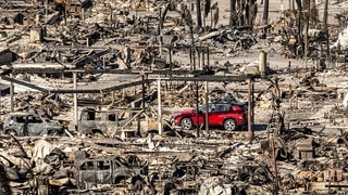 Ein rotes Auto fährt an Häusern und Fahrzeugen vorbei, die durch das Palisades-Feuer in den Pacific Palisades Bowl Mobile Estates zerstört wurden.