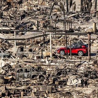 Ein rotes Auto fährt an Häusern und Fahrzeugen vorbei, die durch das Palisades-Feuer in den Pacific Palisades Bowl Mobile Estates zerstört wurden.