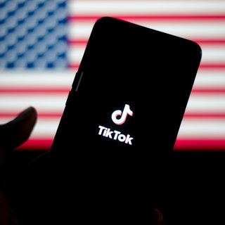 TikTok auf einem Smartphone, im Hintergrund die Flagge der USA. Die App wurde wegen eines Verbots abgeschaltet.