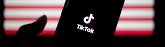 TikTok auf einem Smartphone, im Hintergrund die Flagge der USA. Die App wurde wegen eines Verbots abgeschaltet.