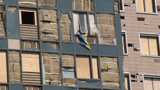 Ein Mann hängt eine Ukraine-Flagge an einem durch russische Raketen teilweise zerstörten Kinderkrankenhaus aus dem Fenster.