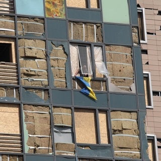 Ein Mann hängt eine Ukraine-Flagge an einem durch russische Raketen teilweise zerstörten Kinderkrankenhaus aus dem Fenster.