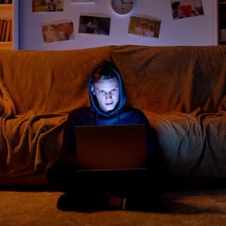 Ein Junge sitzt auf dem Boden am Laptop. In Italien hat sich ein Schüler ins Bildungsministerium gehackt. (Symbolbild)