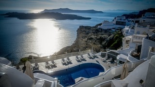 Überblick über Santorini: Man sieht einen Hotelpool und dahinter das Meer vor dunkelblauem Himmel.