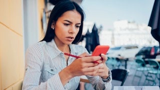 Eine Frau schaut besorgt auf ihr Handy. Die Polizei warnt vor betrügerischen Jobangeboten per Whatsapp.