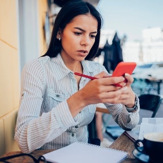 Eine Frau schaut besorgt auf ihr Handy. Die Polizei warnt vor betrügerischen Jobangeboten per Whatsapp.