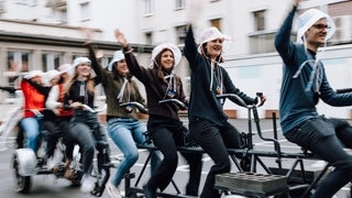 Studierende der Hochschule Mainz sitzen auf einer Fahrradvorrichtung am Oktopus-Wagen für den Rosenmontagszug, mit dem Pfandflaschen gesammelt werden