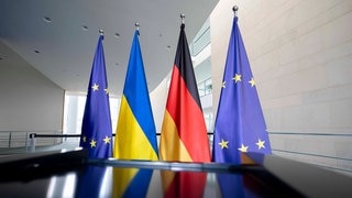 Fahnen der EU, der Ukraine und Deutschlands stehen hinter einem Rednerpult