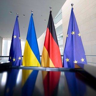 Fahnen der EU, der Ukraine und Deutschlands stehen hinter einem Rednerpult