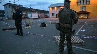 Ein Polizist und ein Soldat stehen am Ort eines Messerangriffs. Nach einem Angriff im elsässischen Mulhouse mit einem Toten und mehreren Verletzten hat die französische Anti-Terror-Staatsanwaltschaft die Ermittlungen übernommen.