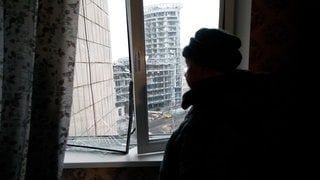 Eine Frau steht an einem Fenster mit Blick auf ein beschädigtes Bürogebäude in Kiew, das durch die Druckwelle eines russischen Raketenangriffs zerstört wurde.