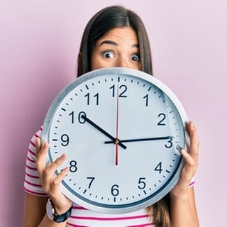 Eine Frau hält eine Uhr vor ihr Gesicht, weil sie weiß, dass im März die Uhren umgestellt werden und weitere Neuerungen auf sie warten