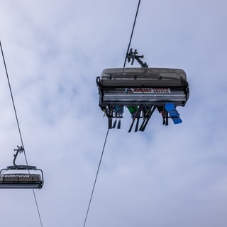 Wintersportler sitzen mit ihren Sportgeräten in einer Sessellift-Gondel der Feldbergbahn und lassen sich den Berg hinaufbringen.