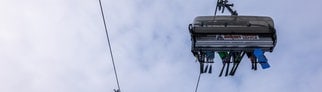 Wintersportler sitzen mit ihren Sportgeräten in einer Sessellift-Gondel der Feldbergbahn und lassen sich den Berg hinaufbringen.