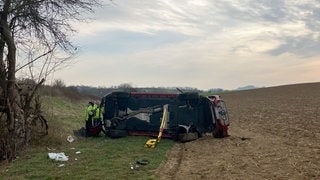 Ein Fahrzeug liegt an der Anschlussstelle Bretzfeld auf der A6 in einem Feld. Bei einem schweren Verkehrsunfall auf der Autobahn 6 östlich von Heilbronn sind zwei Menschen gestorben – vier weitere wurden schwer verletzt.