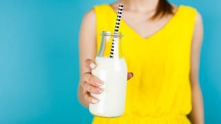 Junge Frau hält eine Milch-Glasflasche mit Strohhalm in der Hand