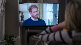 Eine Frau sitzt auf der Couch und schaut das TV-Interview mit Harry.