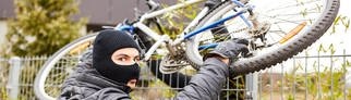 Zwei vermummte Diebe wuchten ein Fahrrad über einen Zaun