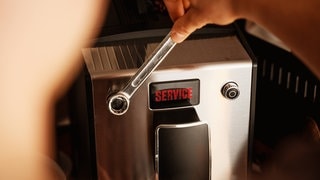 Mann führt den Service mit dem Schraubenschlüssel an der Kaffeemaschine in der Küche durch