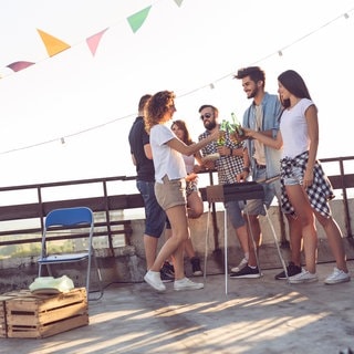 Junge Menschen grillen auf dem Balkon bei abendlicher Sonneneinstrahlung