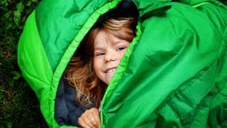 Kleines Kind liegt grinsend auf dem Boden im knallgrünen Schlafsack
