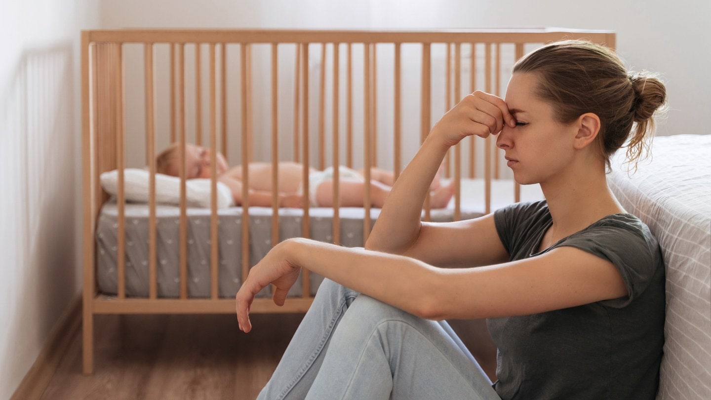 Frau mit Wochenbettdepression sitzt am Boden neben ihrem Baby