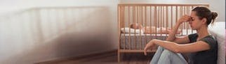 Frau mit Wochenbettdepression sitzt am Boden neben ihrem Baby