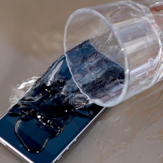 Ein Glas Wasser wird über ein Handy geschüttet.