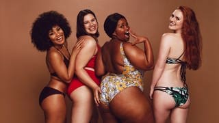 Vier Frauen mit unterschiedlichen Figuren und Hautfarben – lachend und selbstbewusst im Bikini, sie stehen für bodypositivity und brauchen keinen BMI-Rechner.