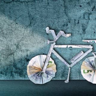 Fahrrad aus Geldscheinen gebastelt vor blauem Hintergrund.