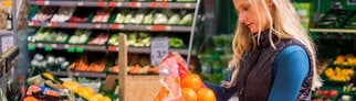 Eine Frau vergleicht in einem Supermarkt ein Netz Orangen