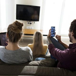 Menschen mit unterschiedlichen technischen Geräten wie Smartphone, Tablet und Fernseher