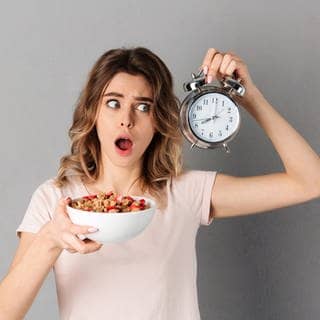 Eine Frau hat eine Uhr in der Hand, damit sie weiß, wann sie essen darf, da sie Intervallfasten macht, um abzunehmen. Wie klären, ob Intervallfasten eine gute Alternative zur klassischen Diät sein kann.