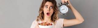Eine Frau hat eine Uhr in der Hand, damit sie weiß, wann sie essen darf, da sie Intervallfasten macht, um abzunehmen. Wie klären, ob Intervallfasten eine gute Alternative zur klassischen Diät sein kann.