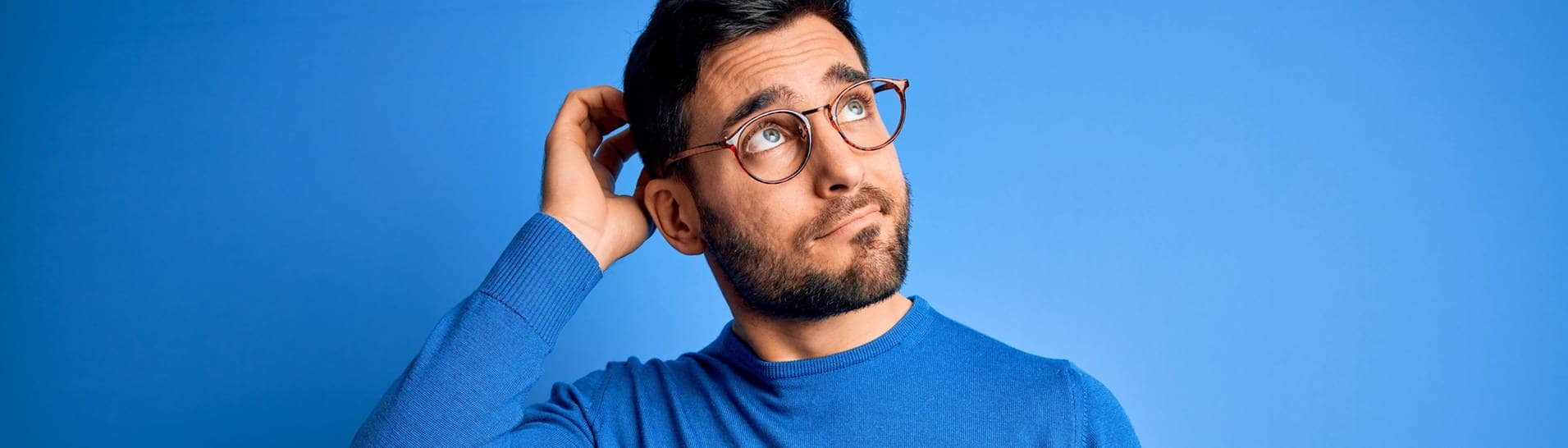 Junger Mann mit Brille und blauem Pullover schaut nachdenkend in die Luft. Symbolbild für Sätze, die du nur verstehst, wenn du Dialekt sprichst.