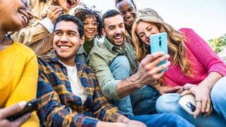 Eine Gruppe junger Menschen schaut gemeinsam auf ein Handy und lacht. Symbolnild für den SWR3-Whatsapp-Kanal.