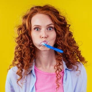 Junge Frau guckt überrascht, die hat eine Zahnbürste im Mund. Symbolbild für Faktencheck: Ist Fluorid in der Zahnpasta giftig?