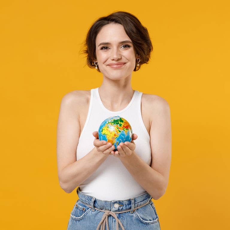 Junge Frau hält lächelnd einen Globus, eine Weltkugel, in der Hand. Symbolbild für 7 deutsche Wörter, die in anderen Sprachen der Welt gesprochen werden.
