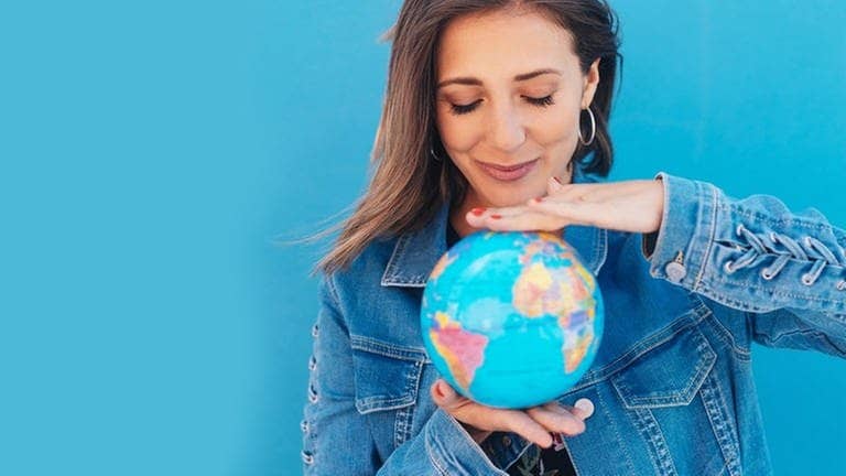 Junge Frau hält eine Weltkugel, einen Globus, zwischen beiden Händen. Symbolbild für deutsche Wörter, die in anderen Sprachen der Welt gesprochen werden.