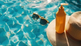 In blauem Pool-Wasser schwimmt eine Sonnenbrille, ein Sonnenhut und eine Flasche Sonnencreme. Symbolbild für Stiftung Warentest Testergebnisse bei Sonnencremes.