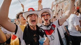 Zwei junge männliche Fans jubeln mit Deutschland-Trikot beim Public Viewing auf dem Schlossplatz in Stuttgart.