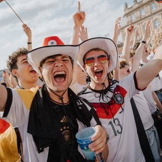 Zwei junge männliche Fans jubeln mit Deutschland-Trikot beim Public Viewing auf dem Schlossplatz in Stuttgart.