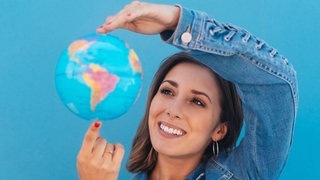 Junge Frau hält einen Globus in der Hand. Symbolbild für deutsche Wörter, die auch in anderen Sprachen vorkommen.