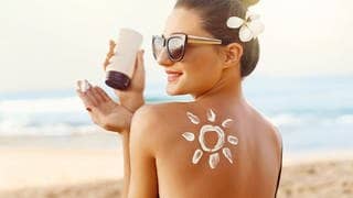 Junge Frau mit Sonnenbrille am Strand. Auf dem Rücken hat sie eine Sonne aus Sonnencreme. Sie lacht. Symbolbild für Stiftung Warentest Sonnencremes.