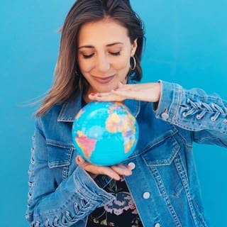Junge Frau hält eine Weltkugel, einen Globus, zwischen beiden Händen. Symbolbild für deutsche Wörter, die in anderen Sprachen der Welt gesprochen werden.