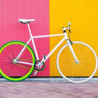 Ein weißes Fahrrad steht vor einer gelb-pinken Wand. 