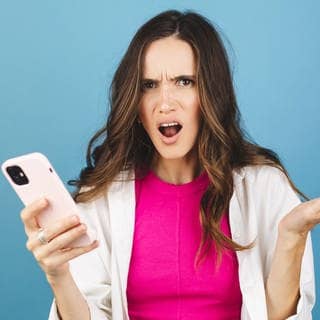 Junge Frau schaut sauer auf ihr Smartphone. Symbolbild für Betrugs-SMS und Whatsapp-Nachrichten mit einem falschen Jobangebot.