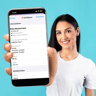 Eine Frau hält ein Smartphone ins Bild, auf dem der Notfallpass auf dem Display zu sehen ist